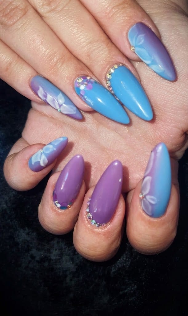Nail art azzurra e lilla con fiori dipinti e strass